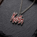 We Rock Korn red glitter logo pendant on a silver-tone metal chain resting on a textured black slate surface