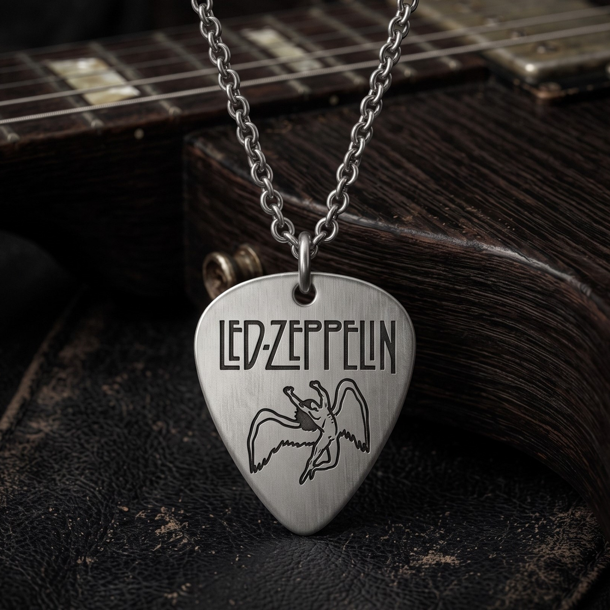 We Rock Led Zeppelin guitar pick necklace in brushed silver hanging over a dark wooden electric guitar body